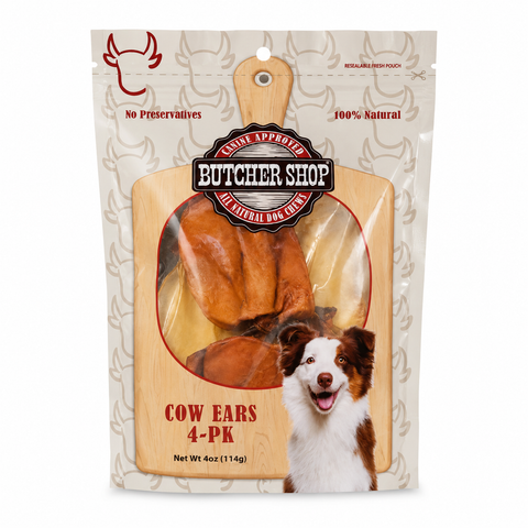 A 4-pack of butcher shop brand cow ears dog treats in a resealable stand-up pouch. The package features a large clear window showing the brown cow ear treats inside, with a wooden cutting board graphic, a dog photo, and red and black text including 'Butcher Shop' and 'Cow Ears 4-Pack'.